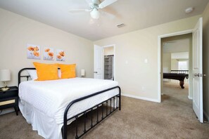 A bedroom with a bed, a nightstand, a ceiling fan, and a door leading to a hallway with a pool table. - Arcade, Billiards with a non heated Pool Two master suites (San Antonio)