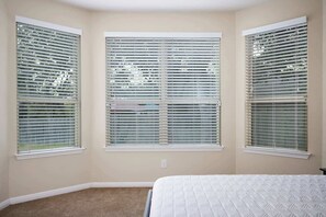 A bedroom with three windows, beige walls, and a white bedspread. - Arcade, Billiards with a non heated Pool Two master suites (San Antonio)