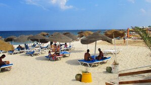 Une plage avec des chaises longues, des parasols et une vue dégagée sur l’océan.