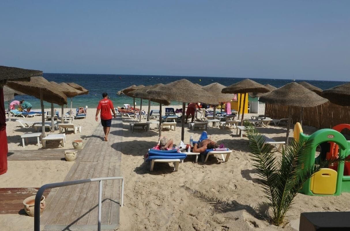A beach with sun loungers, umbrellas, and a wooden walkway.