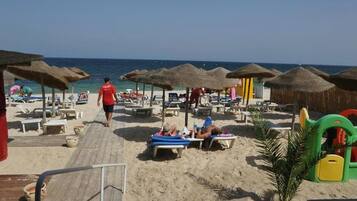 A beach with sun loungers, umbrellas, and a wooden walkway.
