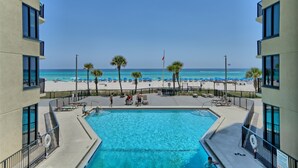 A pool area with a view of the beach, surrounded by palm trees and lounge chairs.