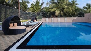 A swimming pool with lounge chairs and a hanging chair, surrounded by palm trees. - Ginger Goa Candolim (Candolim)
