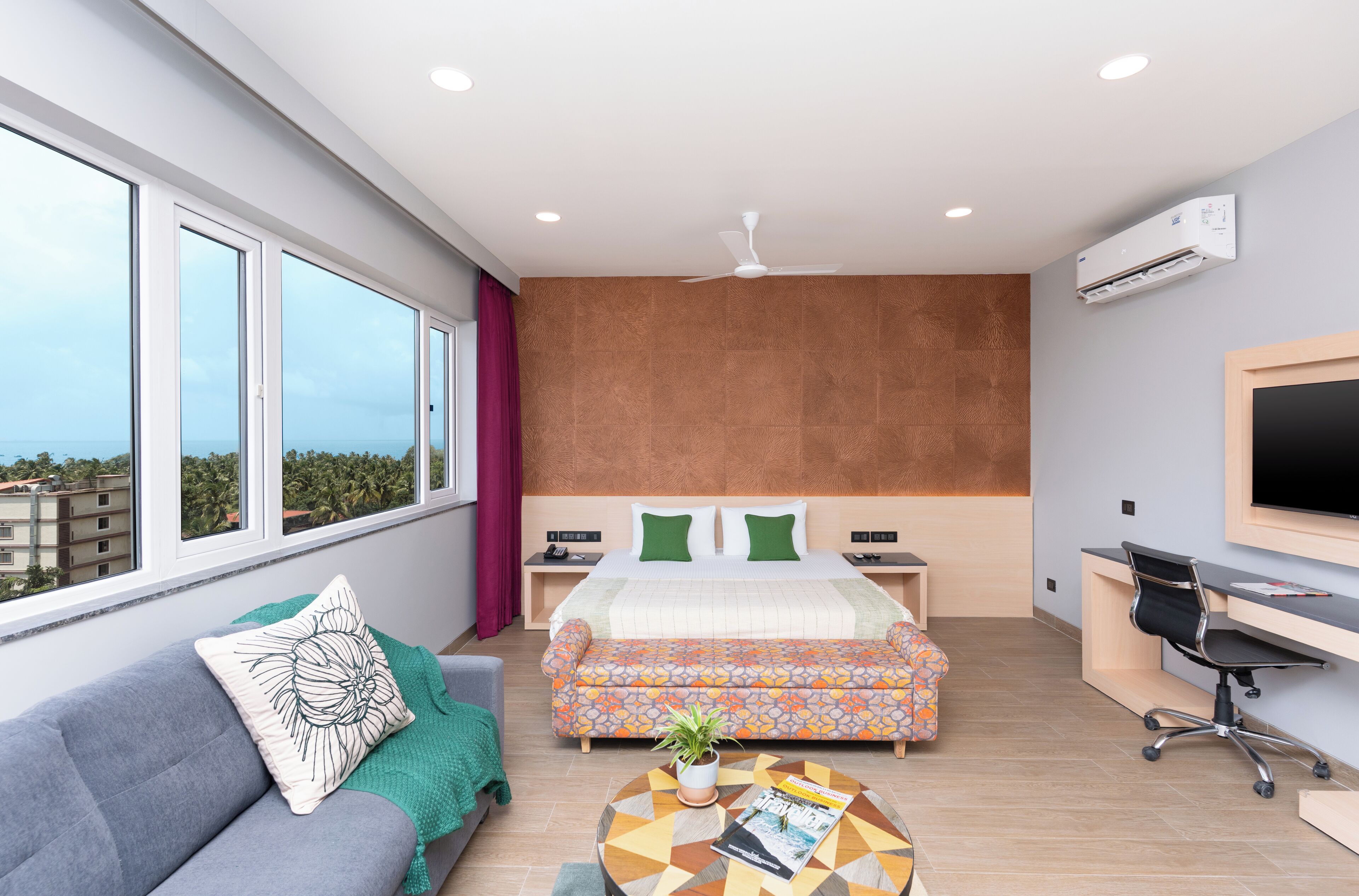 A modern hotel room with a large bed, a sofa, a desk, and a view of the city.