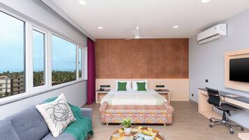 A modern hotel room with a large bed, a sofa, a desk, and a view of the city.