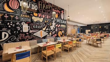 A restaurant with wooden tables and chairs, a black wall with colorful doodles, and a herringbone floor pattern.