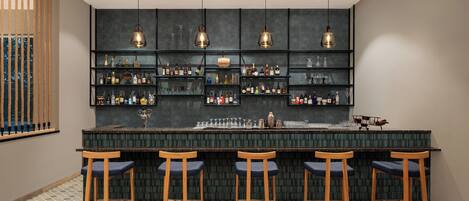 Un área de bar con piso de baldosas oscuras, taburetes de madera y estantes llenos de botellas.