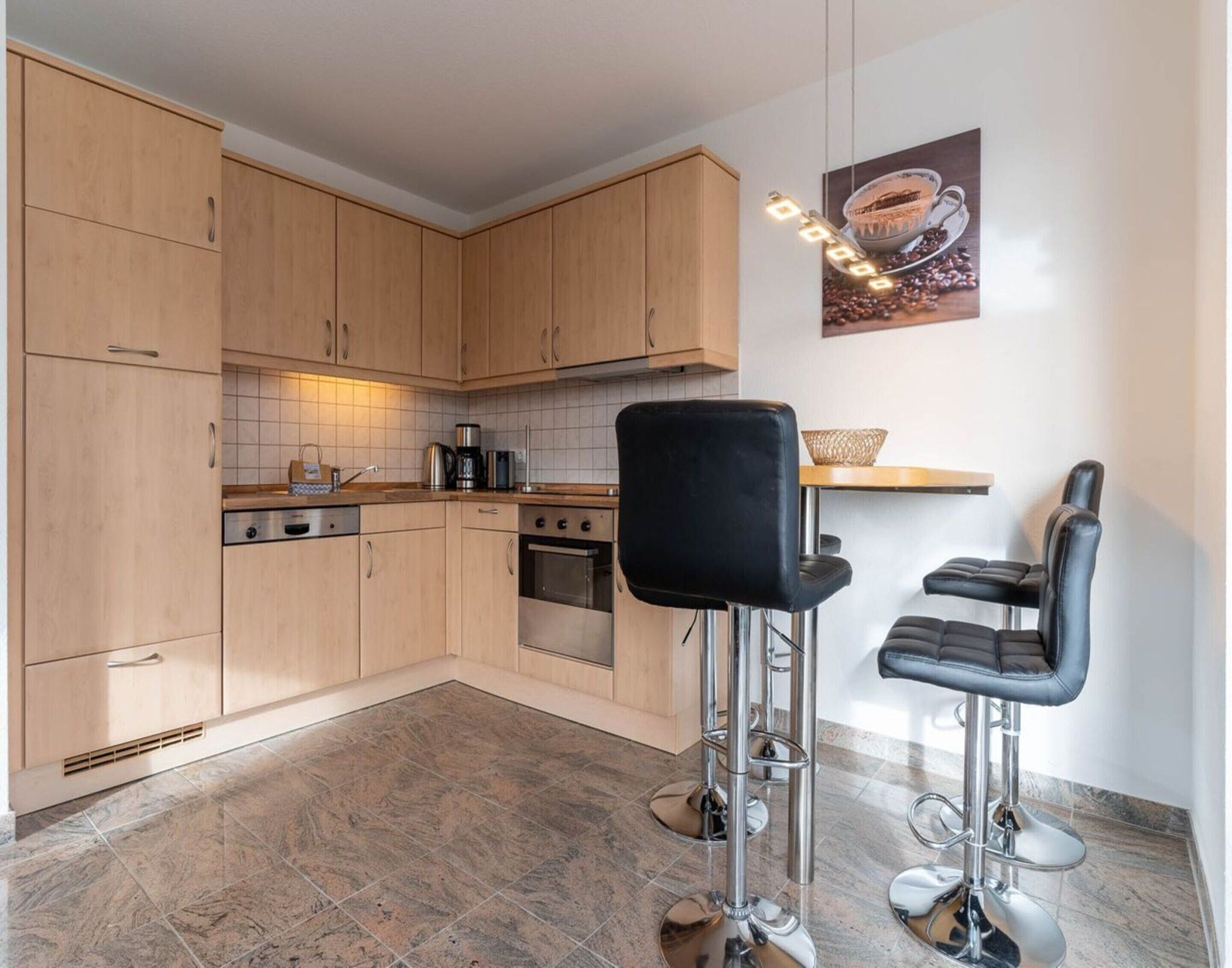 Une cuisine moderne avec des meubles en bois, une cuisinière à gaz et deux tabourets de bar.