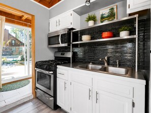 A modern kitchen with white cabinets, a black backsplash, stainless steel appliances, and a view of the outdoors.