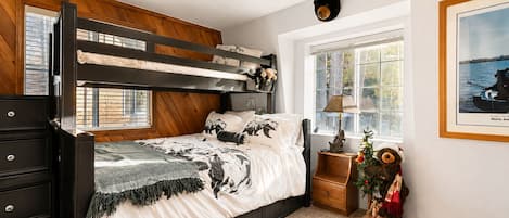 A bunk bed with a wooden headboard, a bedside table with a lamp, a teddy bear, and a framed picture on the wall.