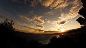 A panoramic view of a sunset over a coastal landscape with silhouettes of trees and a distant cityscape. - Pod Mainowa Propa (Konskie)