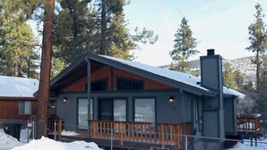 A cabin with a wooden deck, large windows, and a chimney.