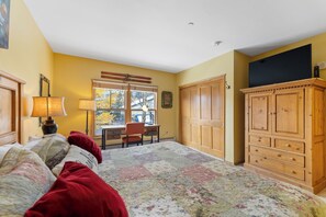 A bedroom with a bed, a desk, a chair, a wardrobe, and a window with a view of trees.