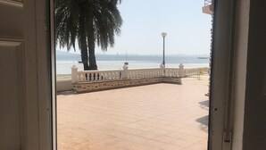 A view from a room to a tiled outdoor area with a white railing, palm trees, and a clear sky.
