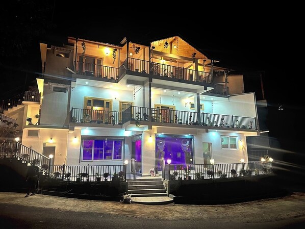 A multi-story hotel with balconies, a central entrance, and a well-lit facade. - Muktkeshii Boutique Resort (Dhari)
