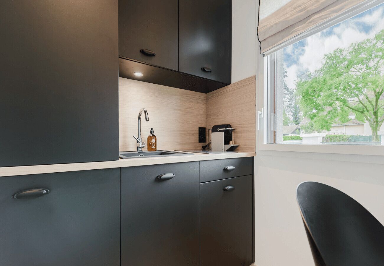 Une cuisine moderne avec des meubles de couleur sombre, un plan de travail en bois et une fenêtre donnant sur un paysage verdoyant.