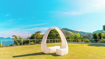 A white, modern sculpture in a grassy field with a clear view of a coastal landscape and hills in the background.