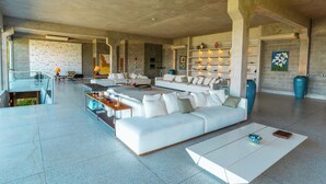 A spacious living area with a large white sofa, a coffee table, and a glass railing overlooking a balcony. - ORLA VILLAS - ANGRA DOS REIS (Angra dos Reis)