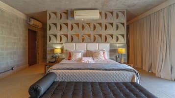 A hotel room with a large bed, a headboard with geometric patterns, an air conditioning unit, and a bedside table with lamps.
