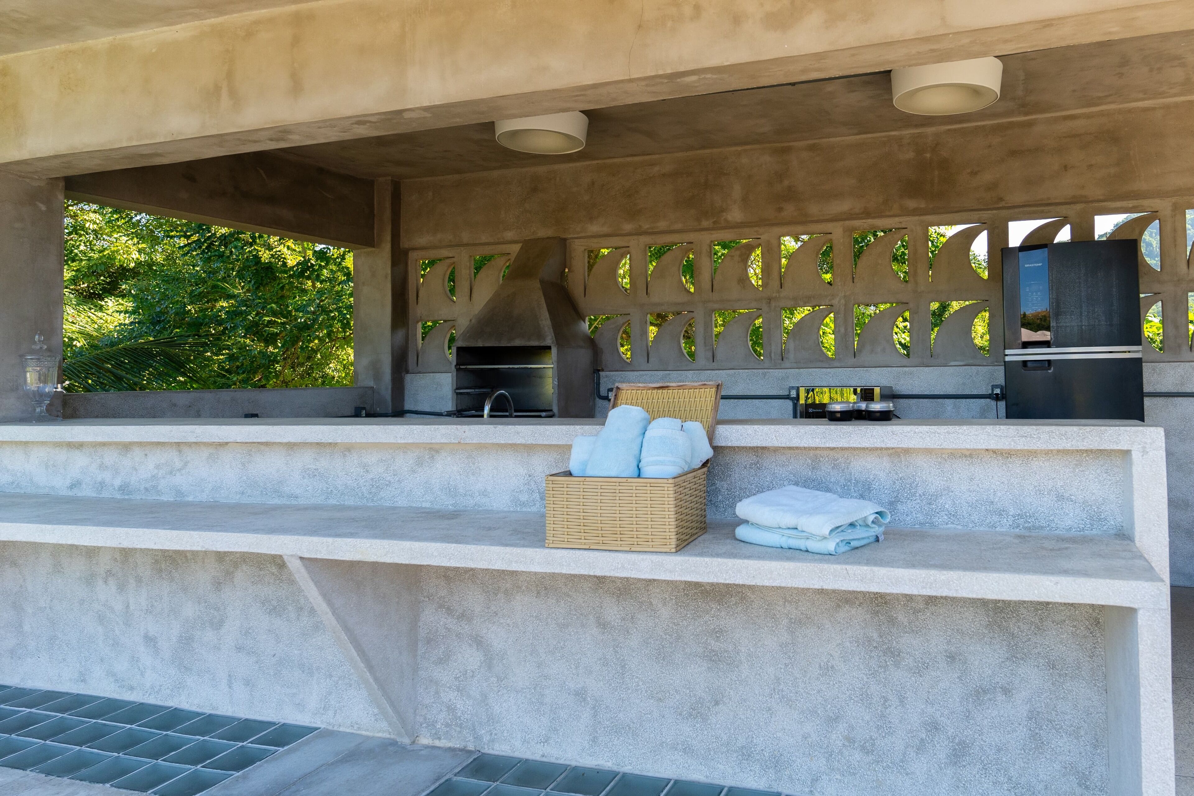 An outdoor kitchen area with a grill, a basket of towels, and a refrigerator.