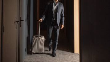 A man in a suit walking through a hotel corridor with a suitcase.