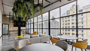 A modern office space with a large window, a sofa, round tables, and hanging plants. - w Majestic 1BR w Stunning Balcony View (Panama City)