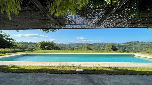 A rectangular swimming pool with clear blue water, surrounded by a grassy area and a paved walkway.