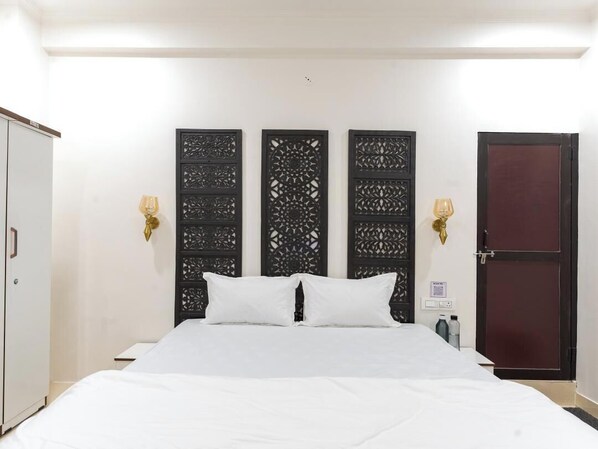 A hotel room with a large bed, a wardrobe, a decorative wall panel, and a door. - Divine Stays (Jaipur)