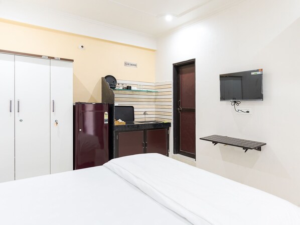 Une chambre d’hôtel équipée d’un lit, d’une armoire, d’un mini-bar, d’une télévision et d’une petite étagère.