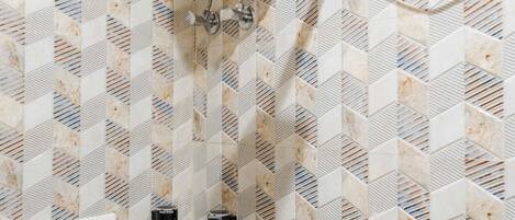 Un baño con ducha, calentador de agua y pared de azulejos con diseño geométrico.