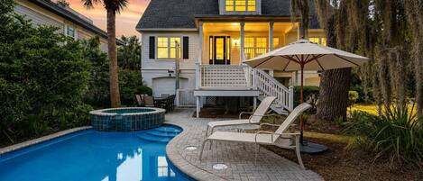 A swimming pool with a hot tub, a covered patio with chairs, and a staircase leading to a second level.