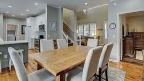 A modern kitchen with white cabinets, a wooden dining table, and a staircase leading to a living area.