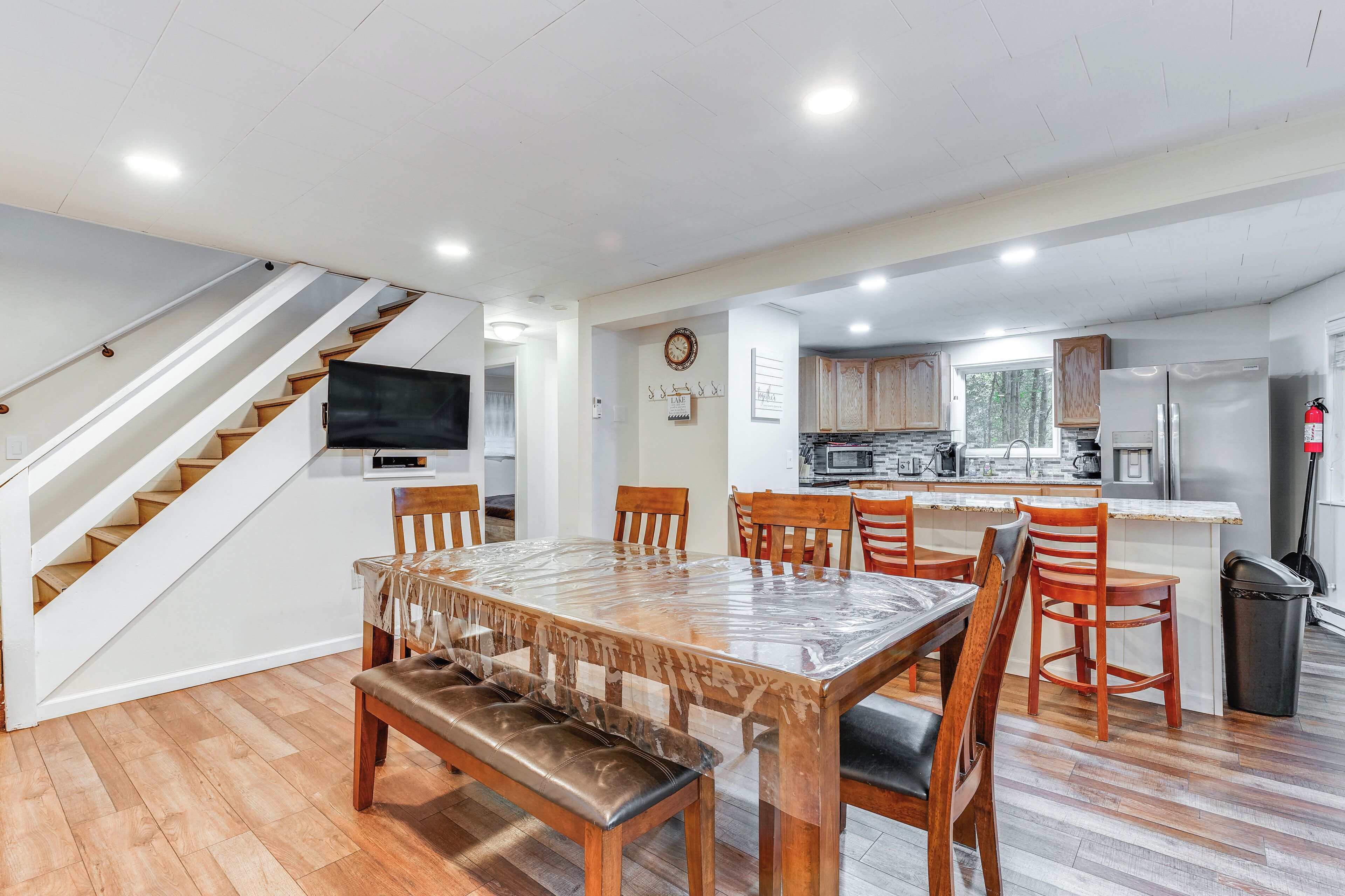 A modern kitchen with a built-in oven, microwave, and refrigerator. There is a dining area with a large wooden table and chairs. A staircase leads to another level.