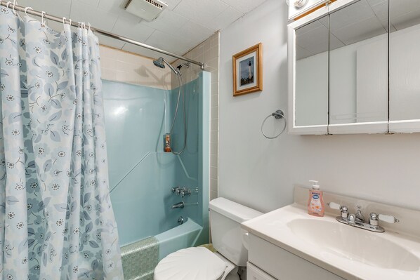 Un baño con ducha, inodoro, lavamanos y un cuadro en la pared.