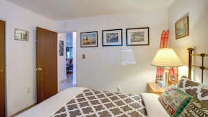 Une chambre à coucher avec une couvre-lit à motifs, une table de chevet avec une lampe et des œuvres d’art accrochées au mur.