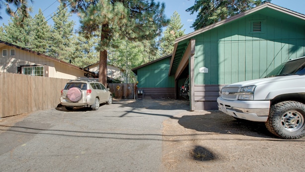 Une allée menant à une résidence, avec deux véhicules garés, un garage et une maison à l’extérieur verdoyante.