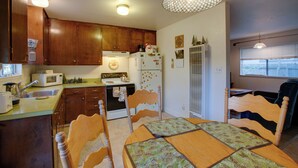 Une cuisine de taille réduite avec des meubles de rangement en bois, une table à manger avec des chaises et un luminaire suspendu.