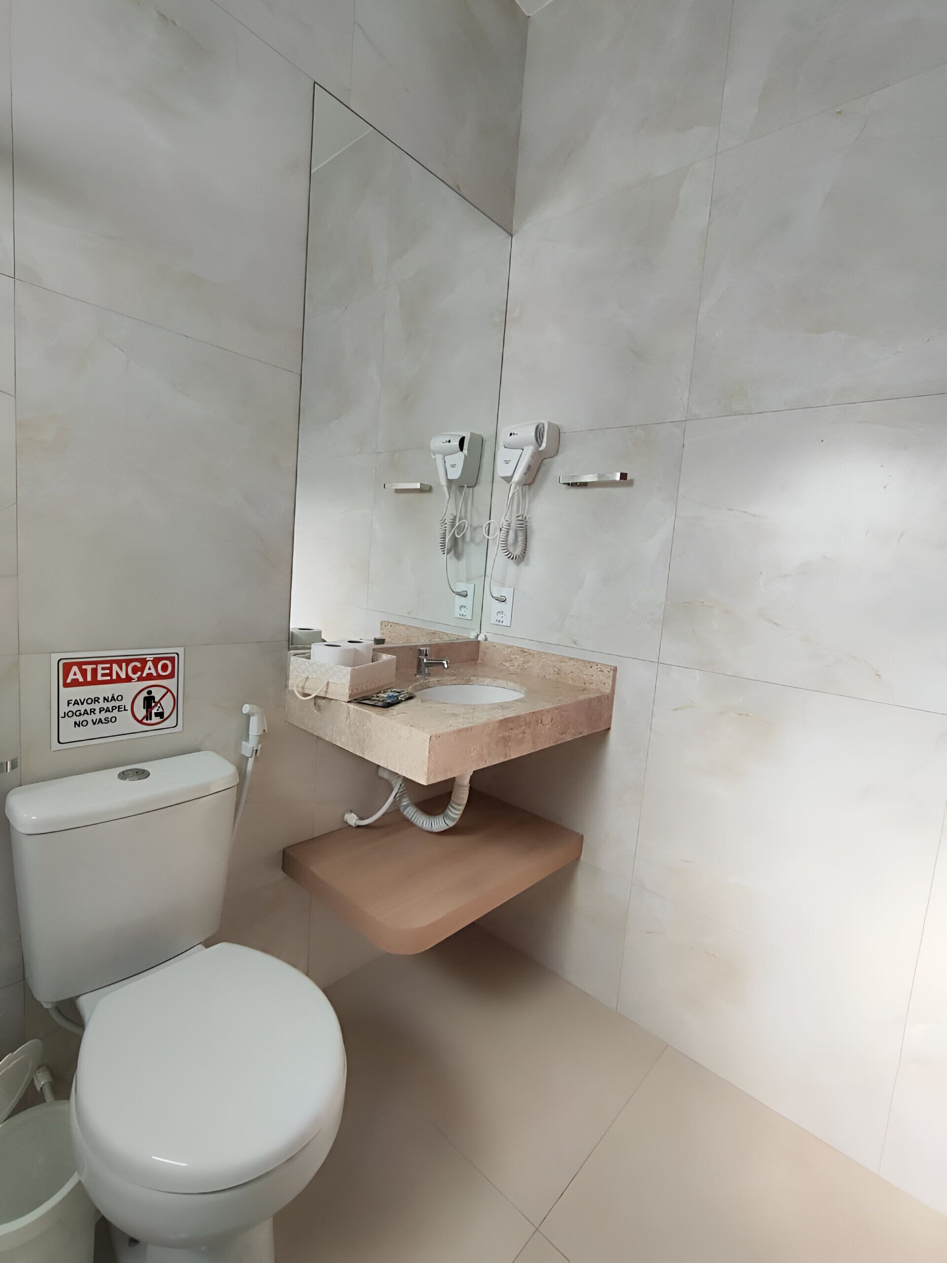 A bathroom with a toilet, sink, and a mirror. There is a sign on the wall and a towel rack.