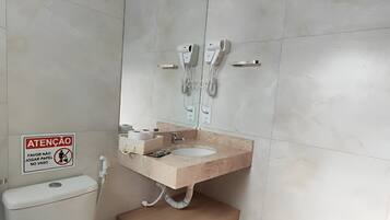 A bathroom with a toilet, sink, and a mirror. There is a sign on the wall and a towel rack.