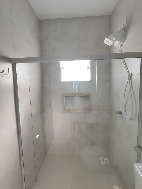 A modern shower with a glass door, a built-in shelf, and a handheld showerhead. - Búzios Suíte Home (Búzios)