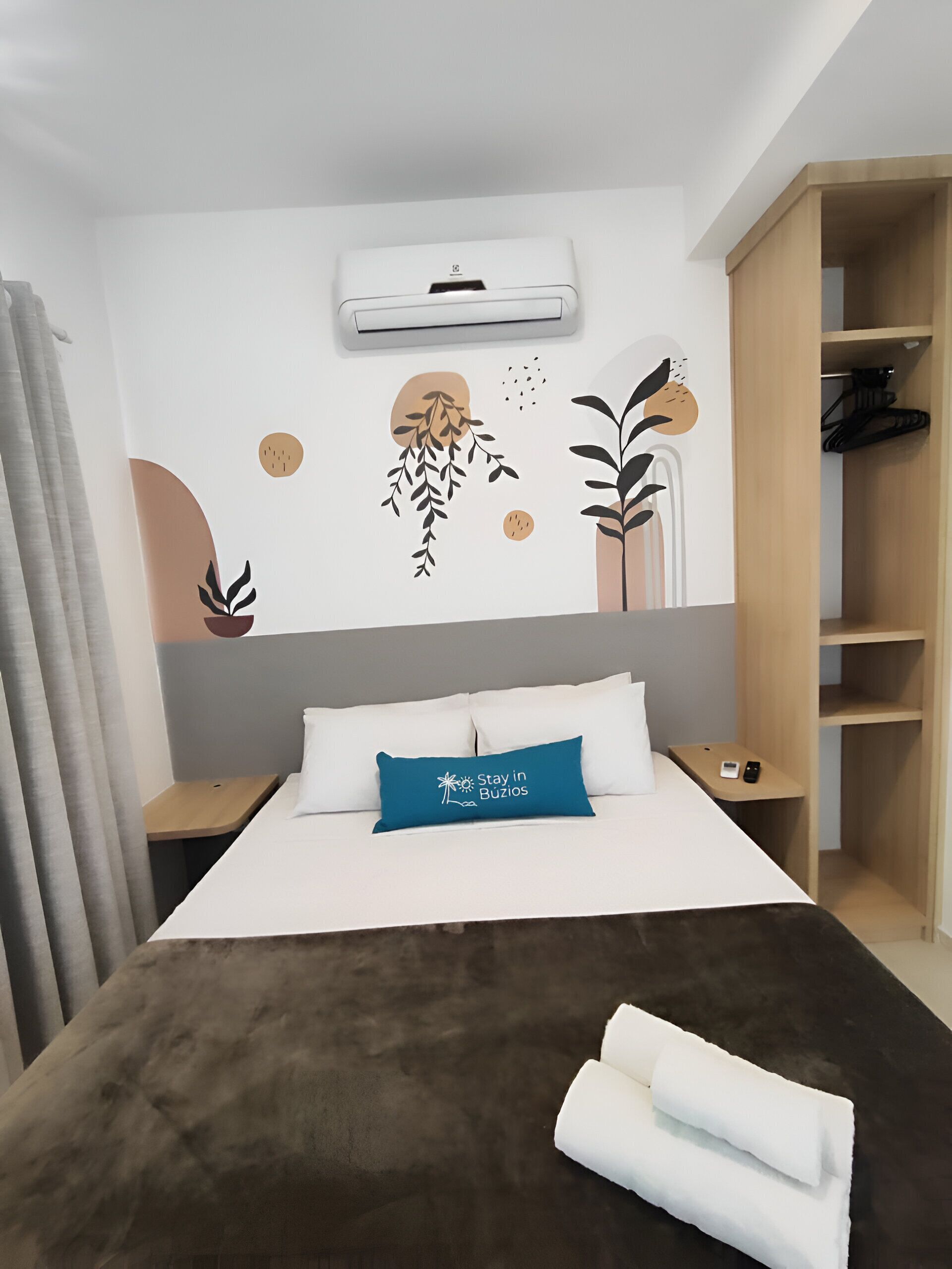 A hotel room with a bed, a blue pillow, a wall-mounted air conditioner, and a wardrobe.