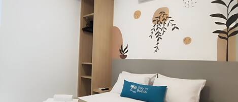 A modern hotel room with a bed, a wardrobe, an air conditioning unit, and wall art.
