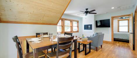 A dining area with a wooden table and chairs, a ceiling fan, and a television mounted on the wall.