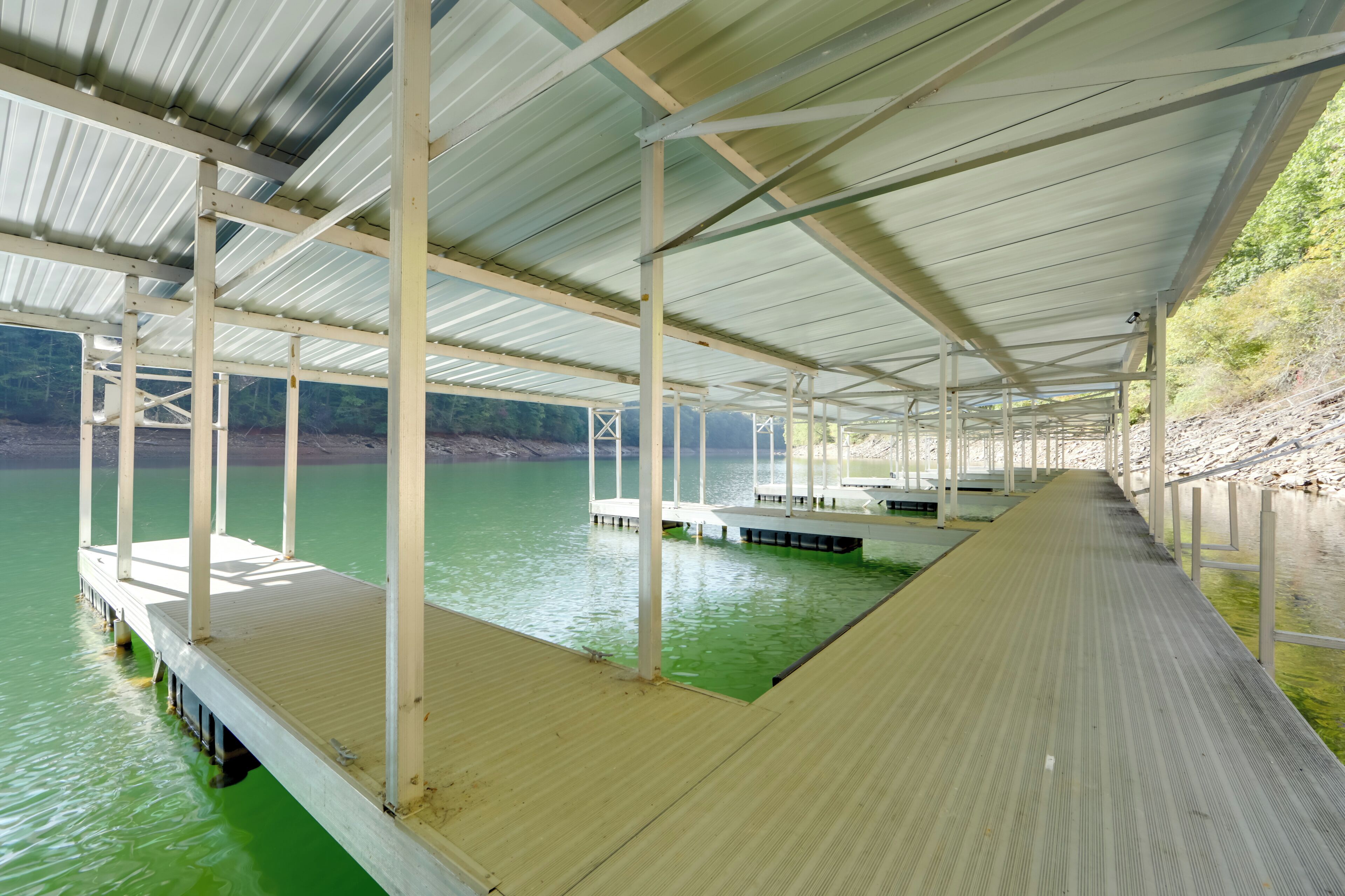 Un muelle techado que se adentra en el agua, sostenido por pilares blancos y un techo de metal.
