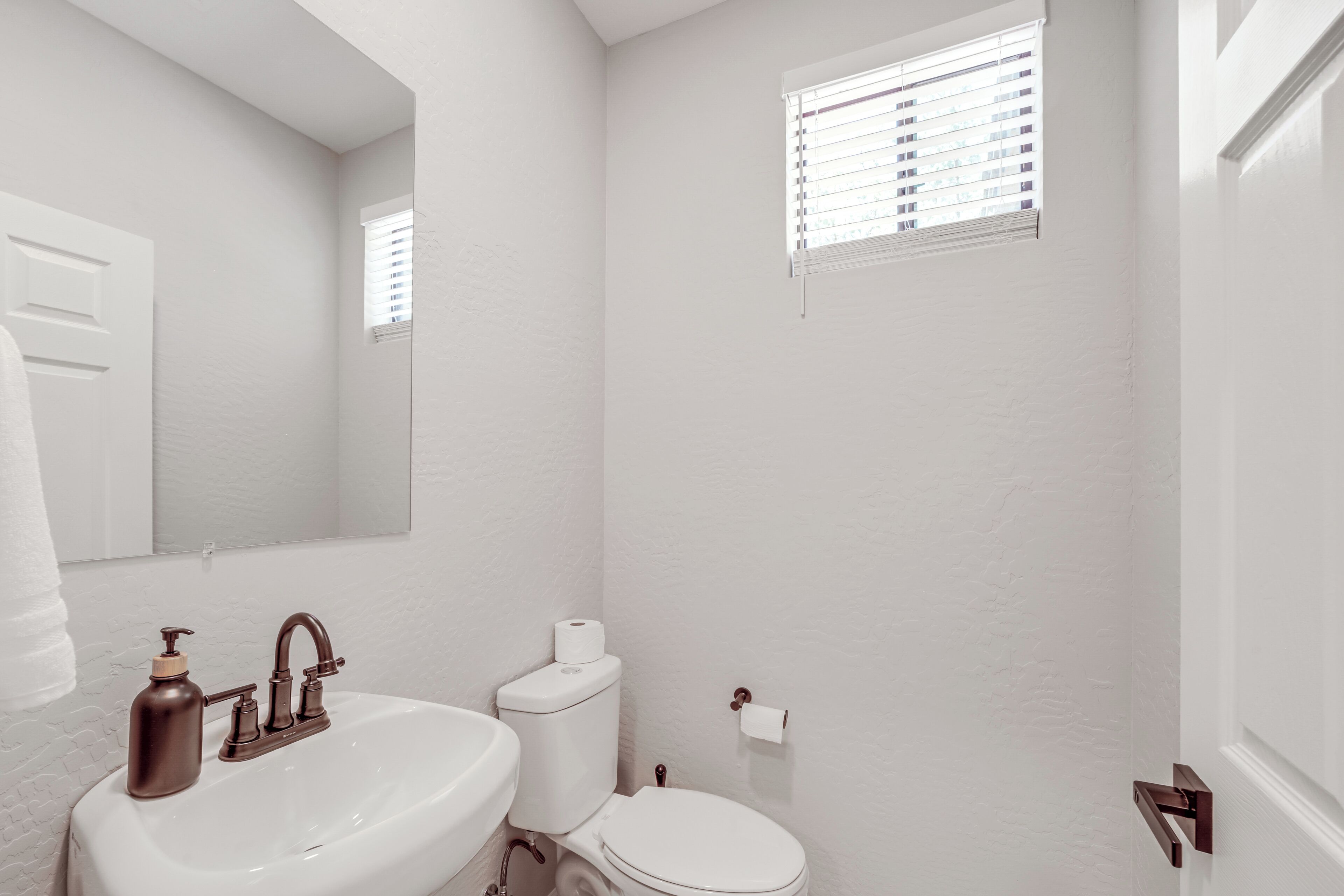 Une salle de bain avec un lavabo blanc, des toilettes et une fenêtre avec des stores.