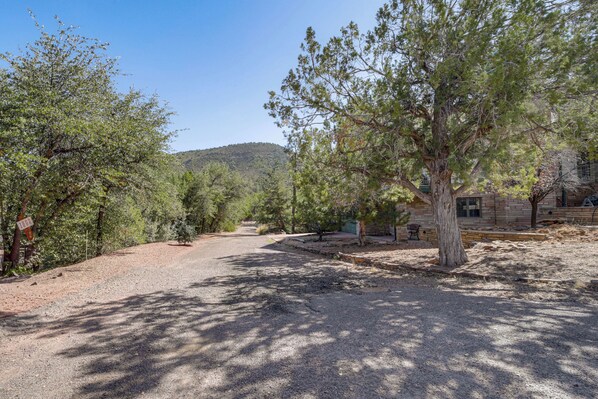 A rural road with trees on both sides, leading to a building with a brick facade. - Games & Outdoor Seating: Cabin in Scenic Payson! (Payson)