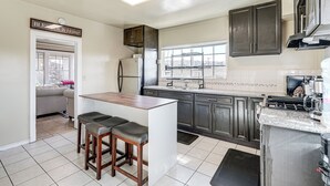 A kitchen with dark cabinets, a central island with stools, a refrigerator, and a window overlooking the city. - Oakland Apartment: 8 Mi to Dtwn! (Oakland)