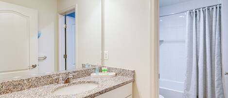 A bathroom with a granite countertop sink, a mirror, and a shower curtain.