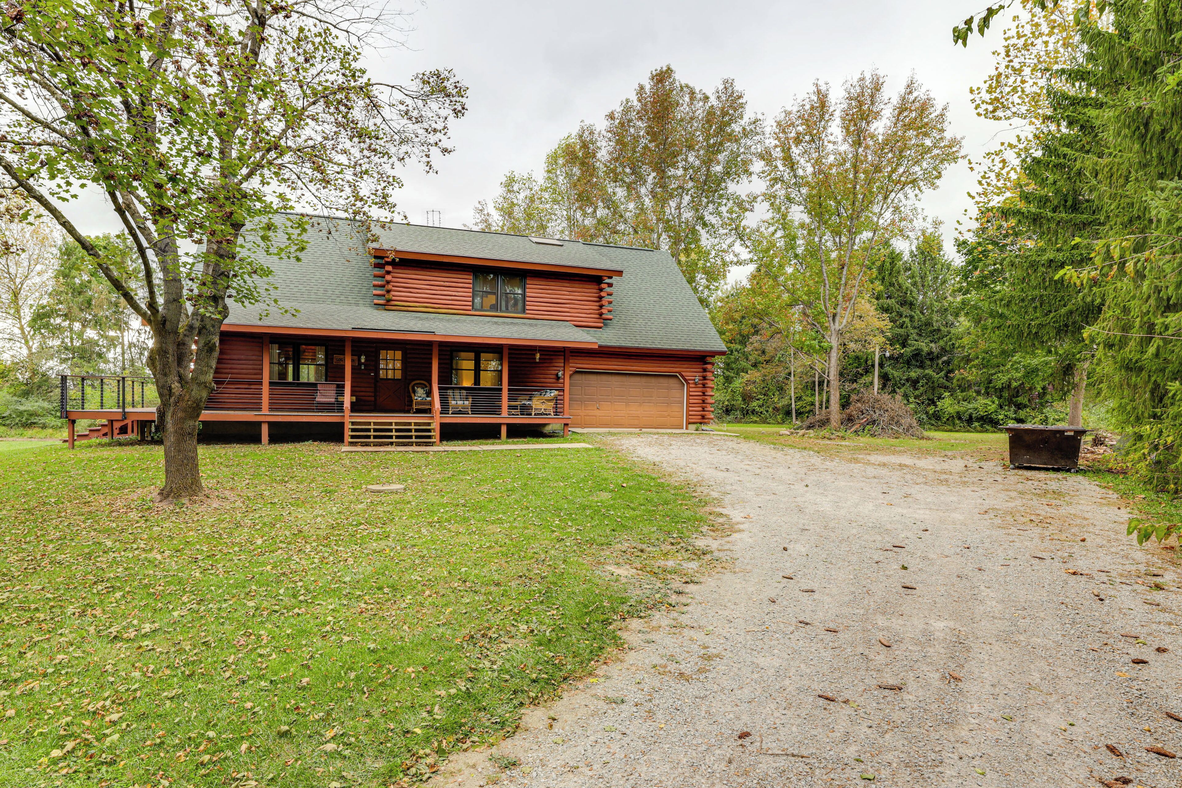 A log cabin with a porch, a garage, and a gravel driveway.