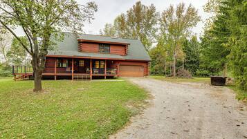 A log cabin with a porch, a garage, and a gravel driveway.